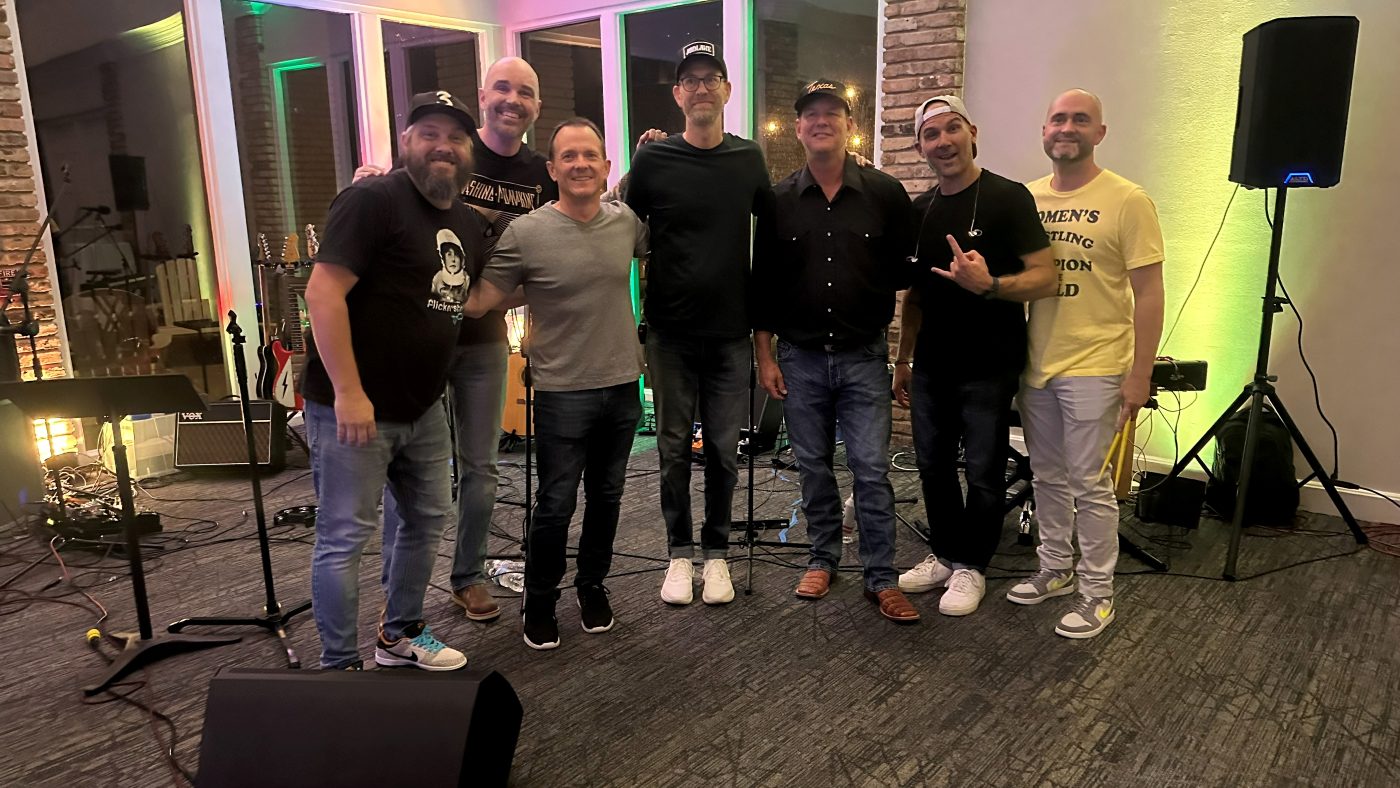 The band posing together after an indoor show, lit by green and pink uplights.