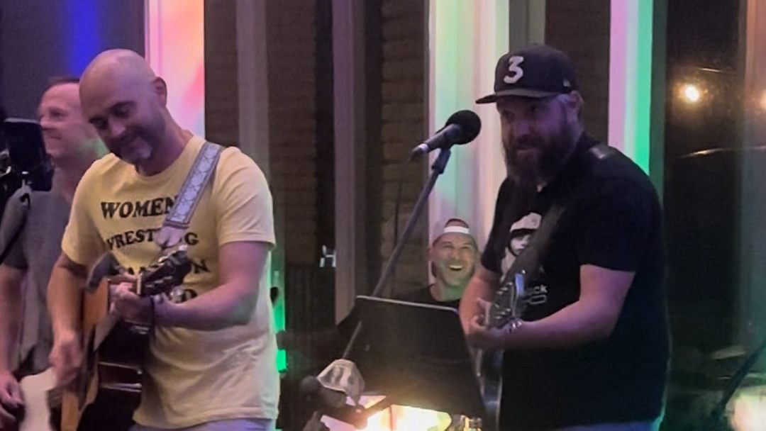 Rhylan on acoustic guitar next to Tobin, with Tom laughing in the background.